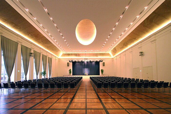 Salle de banquet élégante au Maritim Hotel Fulda avec scène, éclairage raffiné et sièges pour événements.