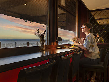 Guest enjoying a drink by the window with a sunset view at Maritim Hotel Travemünde