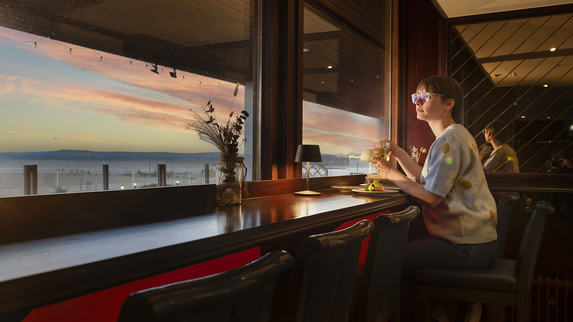 Guest enjoying a drink by the window with a sunset view at Maritim Hotel Travemünde
