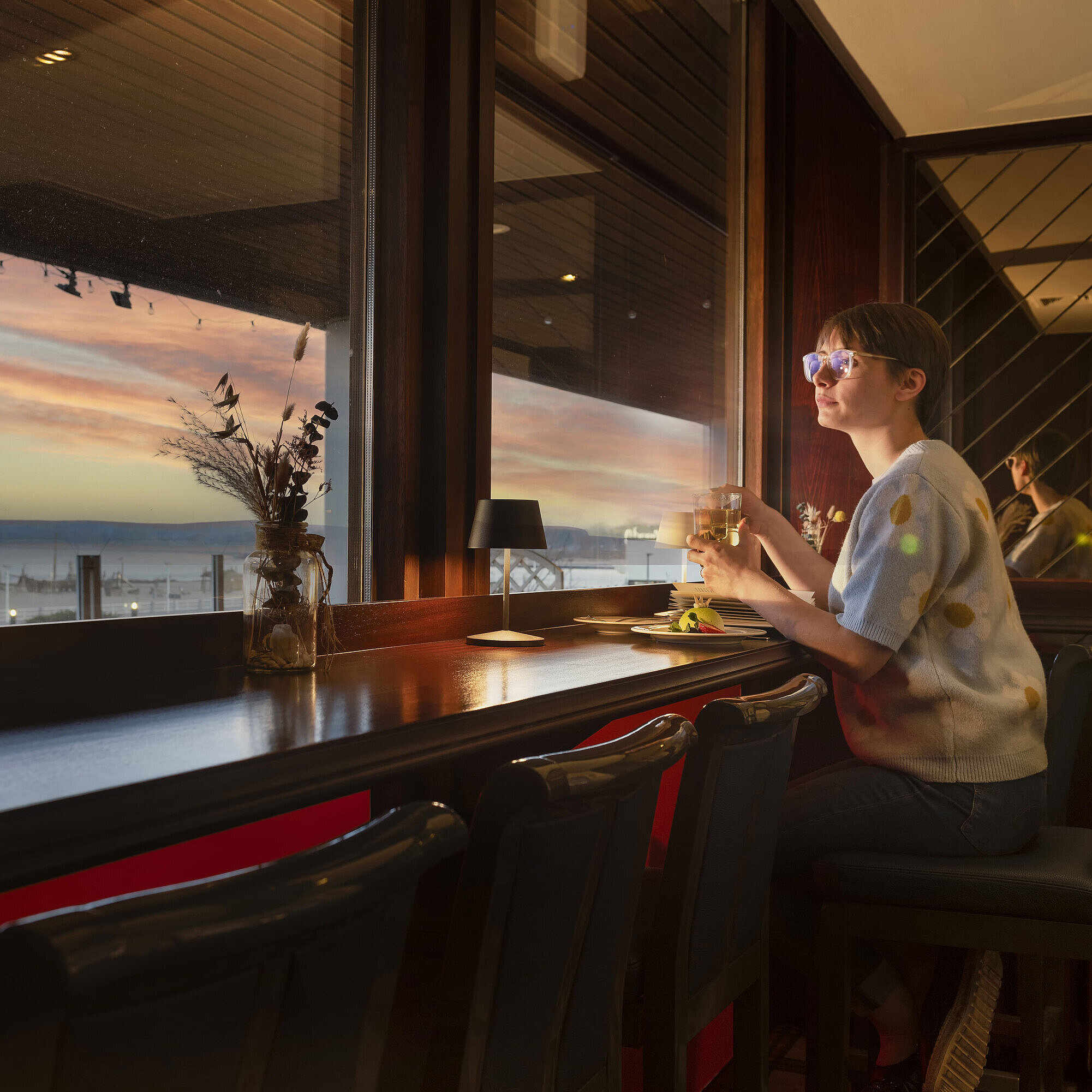 Guest enjoying a drink by the window with a sunset view at Maritim Hotel Travemünde