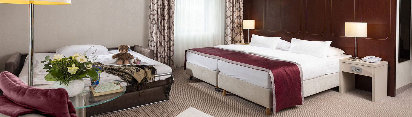 Habitación familiar Comfort en el Hotel Maritim Bonn con cama doble, sofá cama, sillón y arreglo floral.