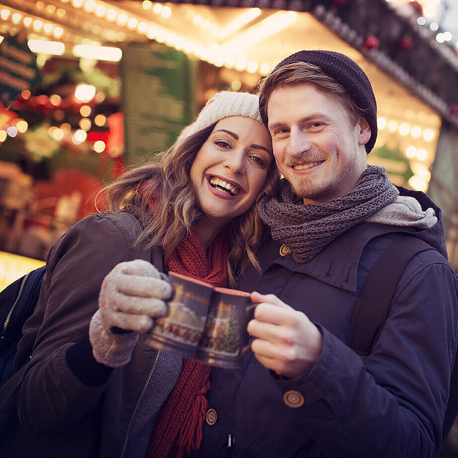 Couple enjoying mulled wine together at a festively lit Christmas market