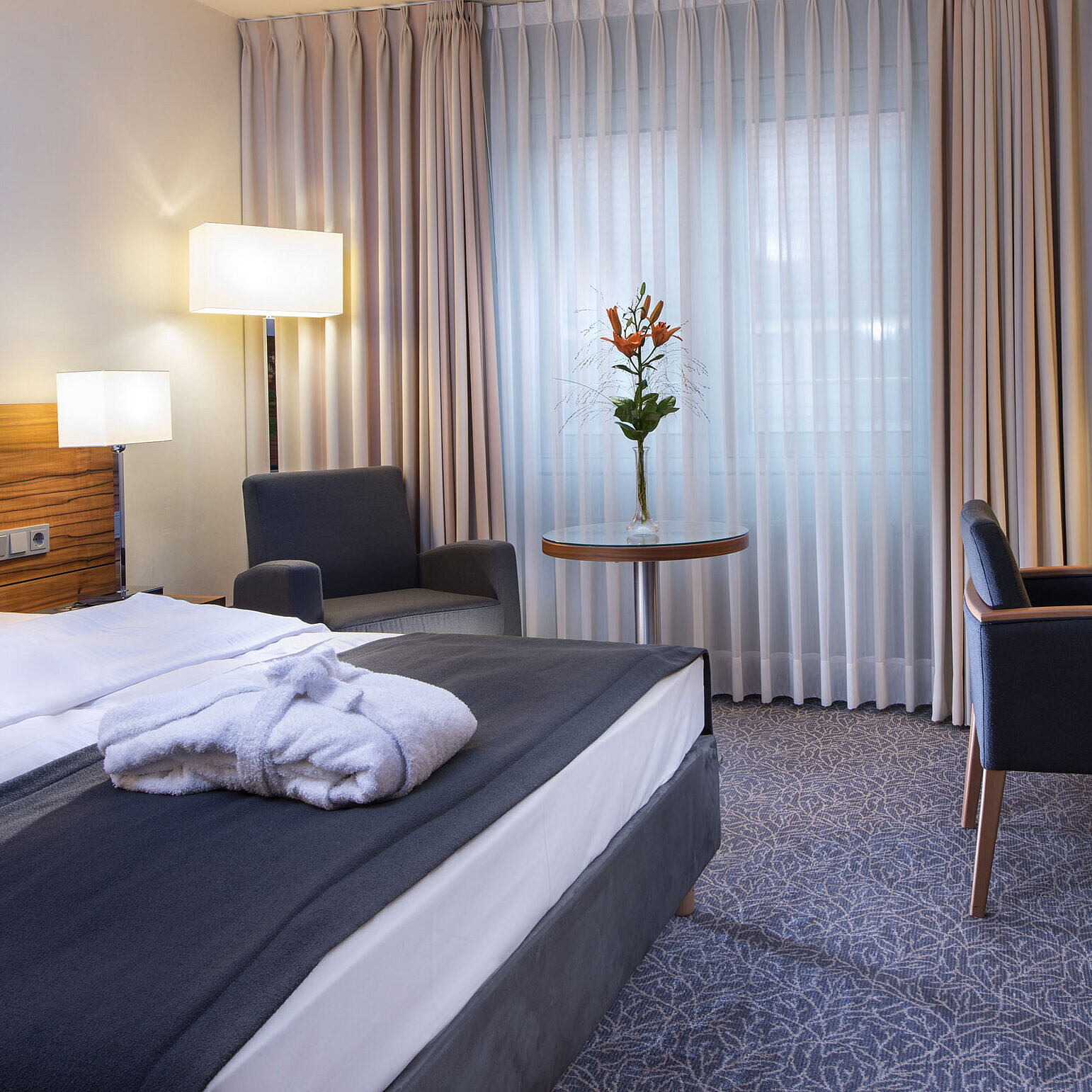 Moderna camera matrimoniale presso il Maritim Hotel Monaco. Dotata di comfort con letto grande, area lavoro e poltrona.