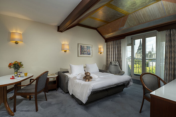 Cozy family room at Maritim Hotel Cologne with a view of Cologne Cathedral and stuffed animals on the bed.