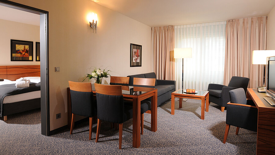 Spacious suite with living room, dining table and separate bedroom at Maritim Hotel Munich