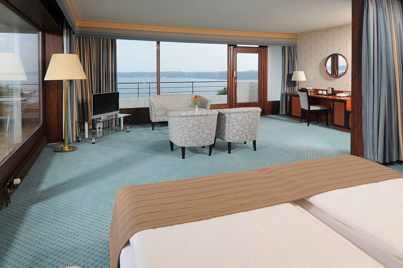 Junior Suite au Maritim Hotel Kiel, avec coin salon, bureau, TV et grande baie vitrée avec vue sur la mer.