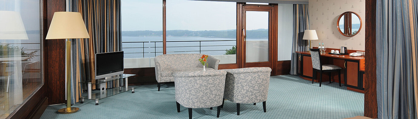 Junior Suite del Maritim Hotel Kiel, con area salotto, scrivania, TV e ampia finestra frontale con vista sul mare.