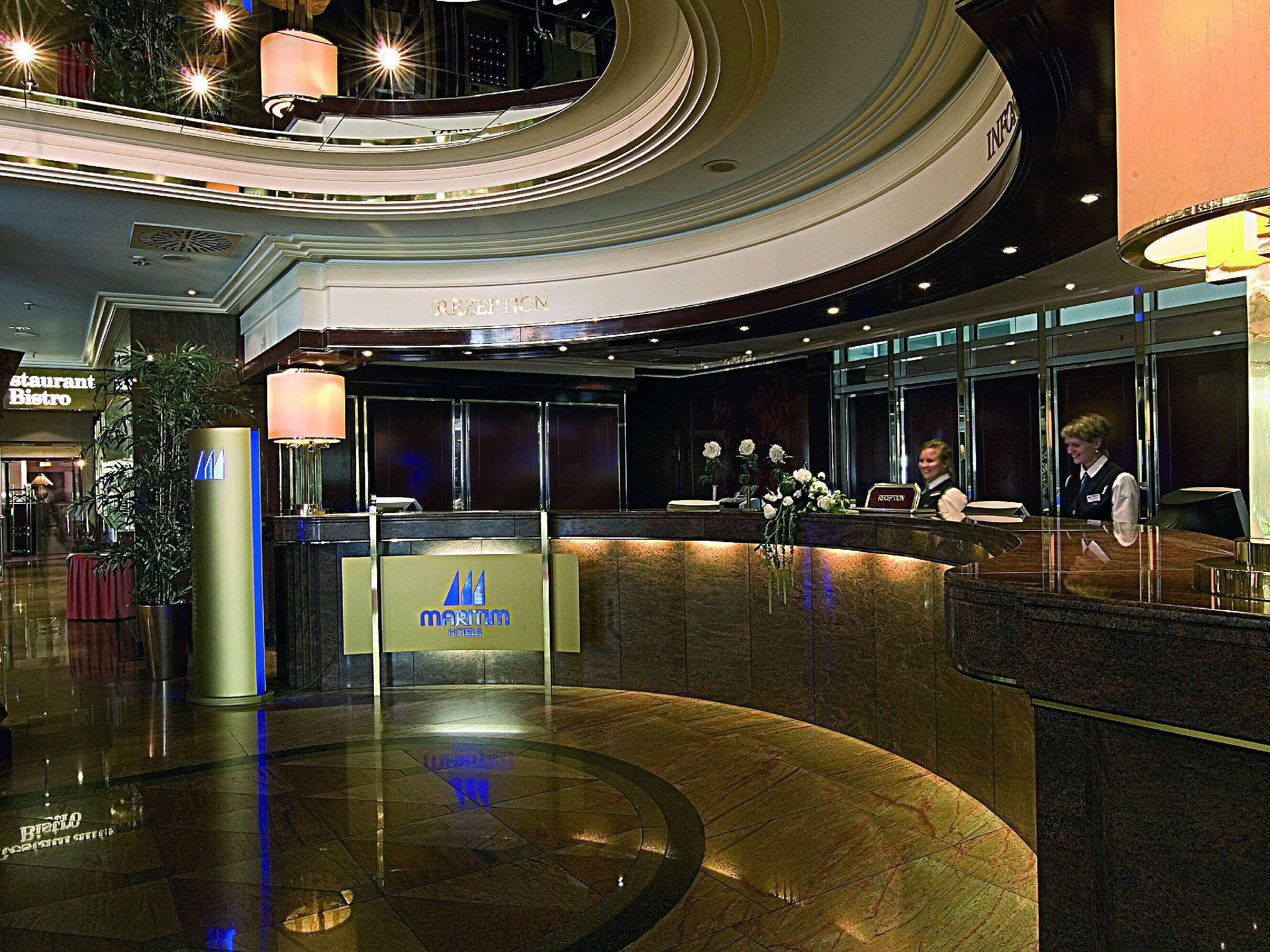 Elegant lobby at the Maritim Hotel Munich with a curved reception desk, marble floor, and friendly staff.