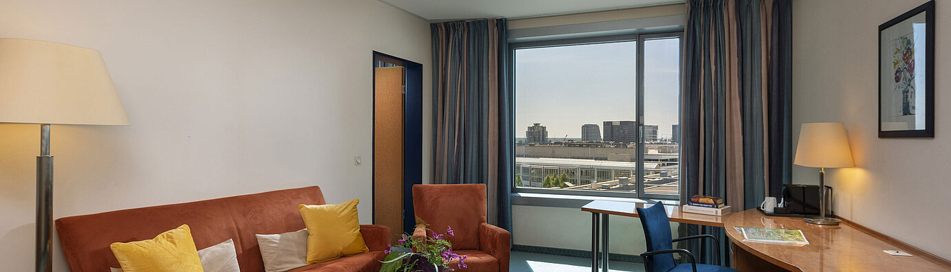 Junior Suite en Maritim Hotel Frankfurt con sala de estar independiente, sofá, escritorio y vista panorámica a la ciudad.