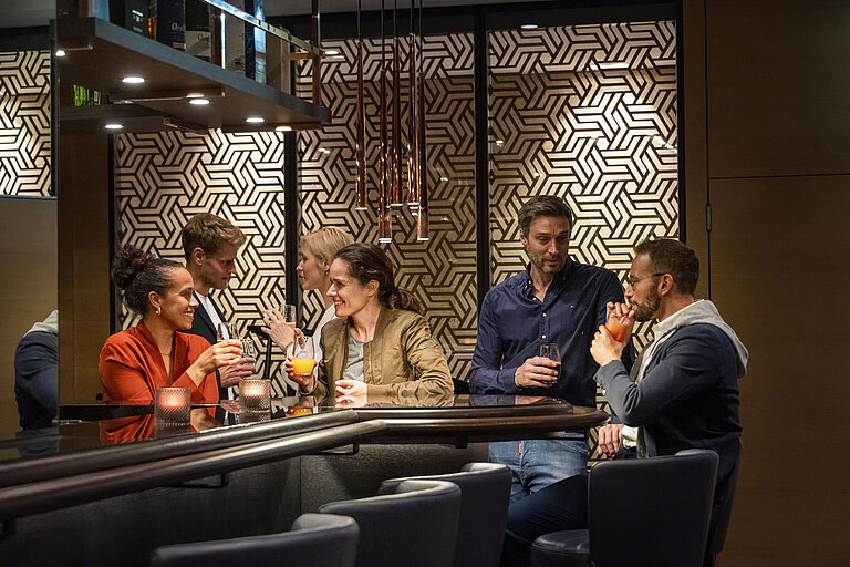 Des clients profitent de boissons et de conversations animées au bar élégant du Maritim Hotel Ingolstadt.