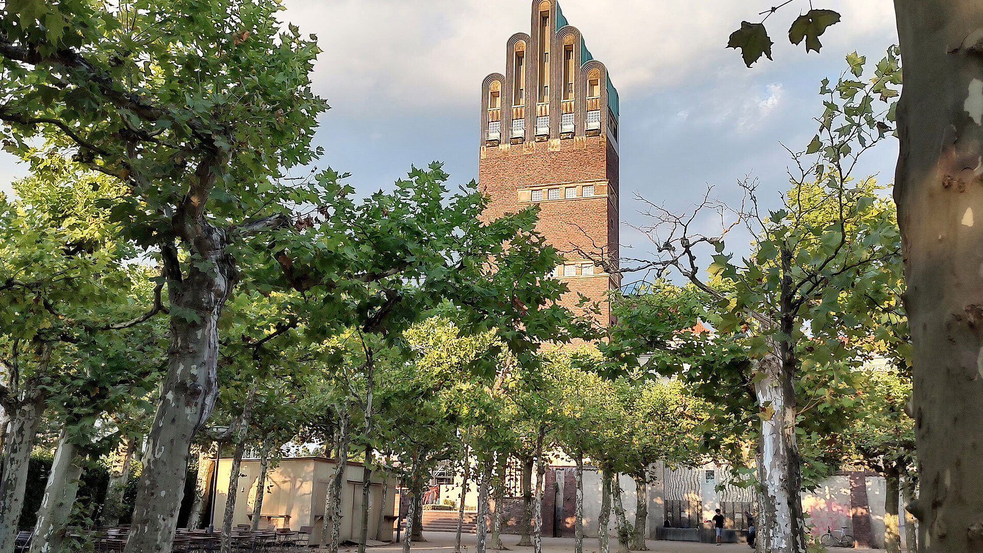 View of the Wedding Tower on Mathildenhöhe in Darmstadt, surrounded by plane trees and blue sky.