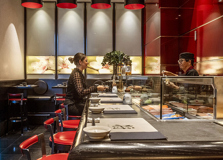 Cliente disfrutando de sushi fresco en el elegante bar de sushi "SushiSho" del Maritim Hotel Düsseldorf con ambiente auténtico