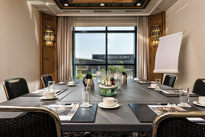 Sala de reuniones luminosa con mesa de conferencias, bebidas y vista al aeropuerto en el Maritim Hotel Hannover.