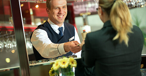 Un barman che porge un drink a un ospite al bar dell'Hotel Maritim con un sorriso amichevole.