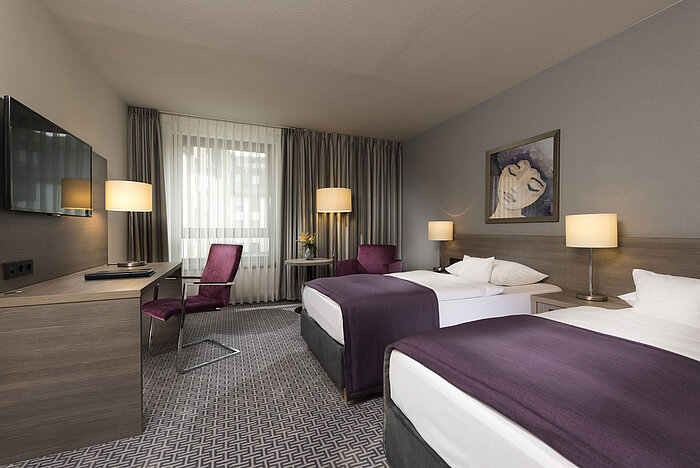 Habitación doble moderna del Maritim Hotel Königswinter con dos camas, escritorio y decoración elegante.