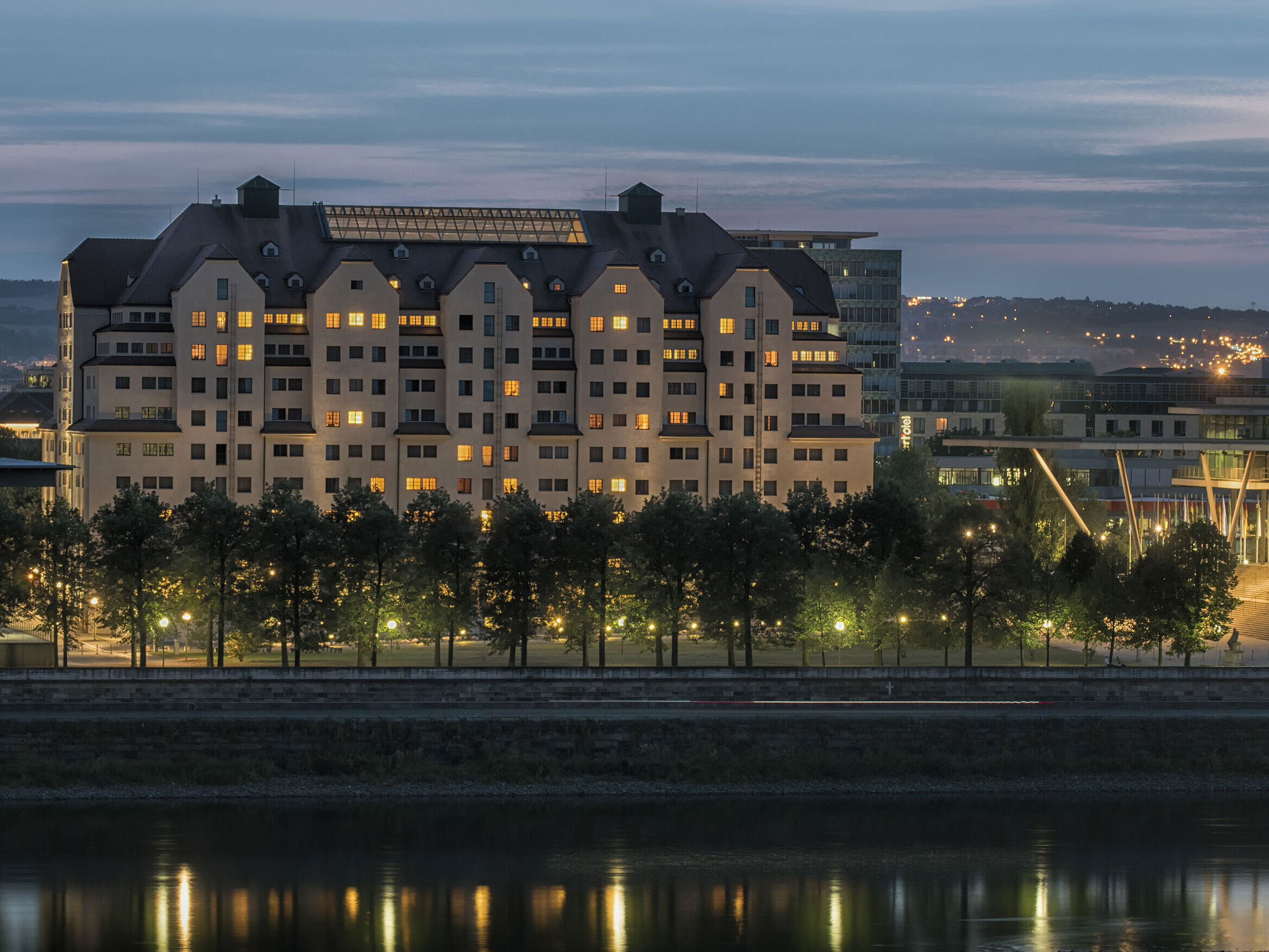 Hôtel Maritim de Dresde illuminé au crépuscule avec des lumières se reflétant sur l'Elbe.