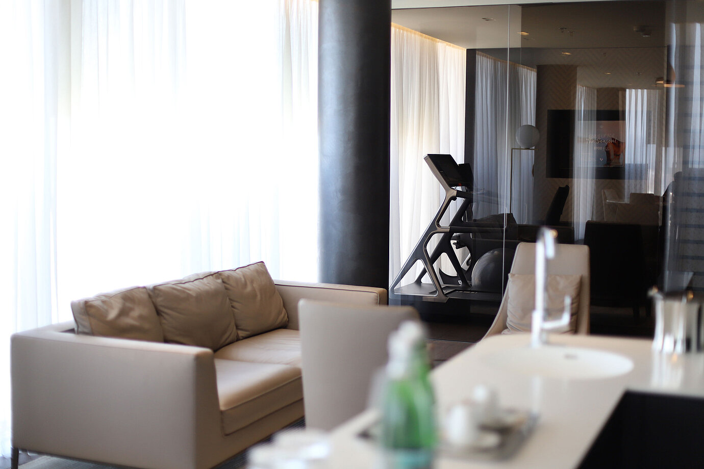 Seating area with beige sofa and view of gym with treadmill behind glass at Maritim Hotel Plaza Tirana