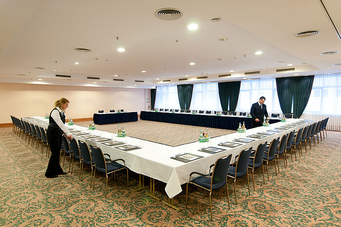 Salle de réunion au Maritim Hotel Magdeburg avec sièges en U, tables dressées et préparation du personnel.