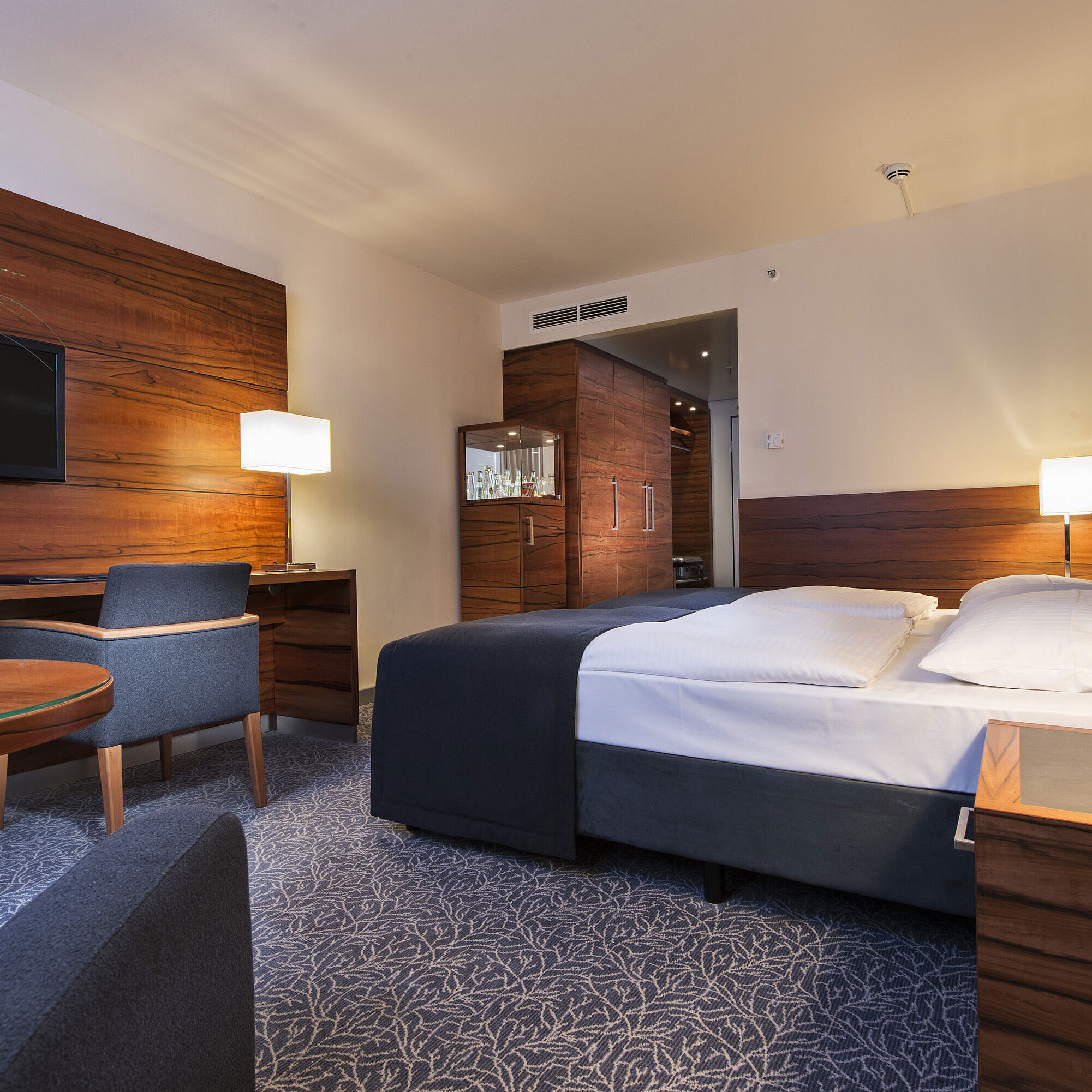 Comfort room Furnished hotel room at the Maritim Hotel Munich with a comfortable bed, workspace, TV, and wood paneling.
