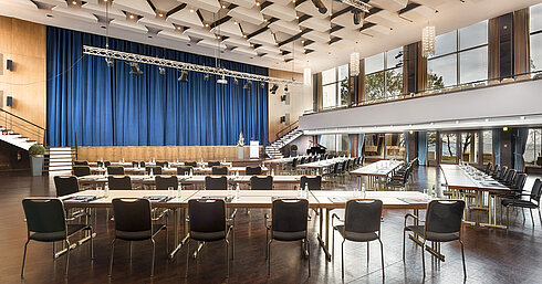 Gran sala «Maritim» en el Maritim Seehotel Timmendorfer Strand con escenario, cortinas azules y asientos para reuniones.