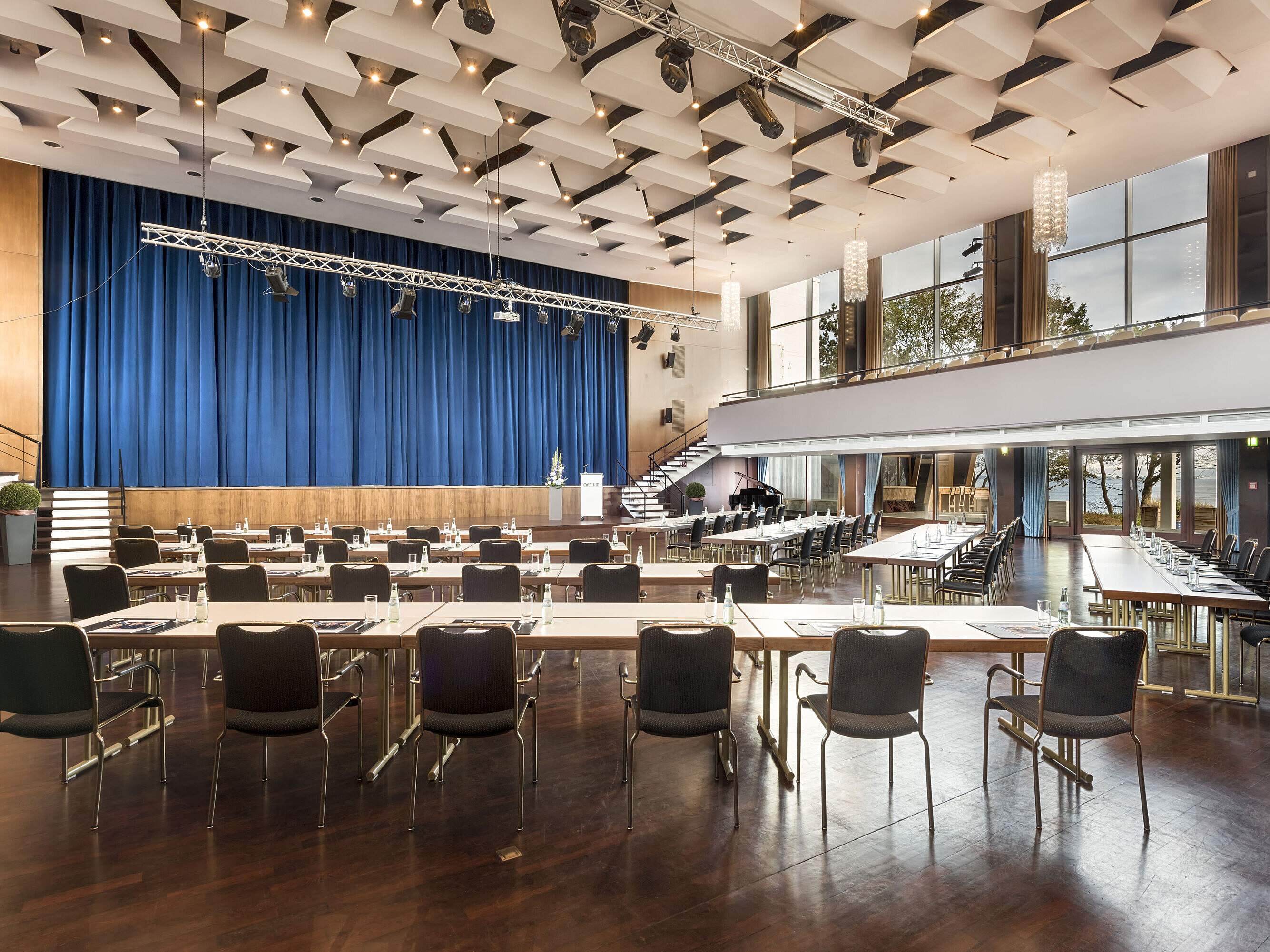 Gran sala «Maritim» en el Maritim Seehotel Timmendorfer Strand con escenario, cortinas azules y asientos para reuniones.