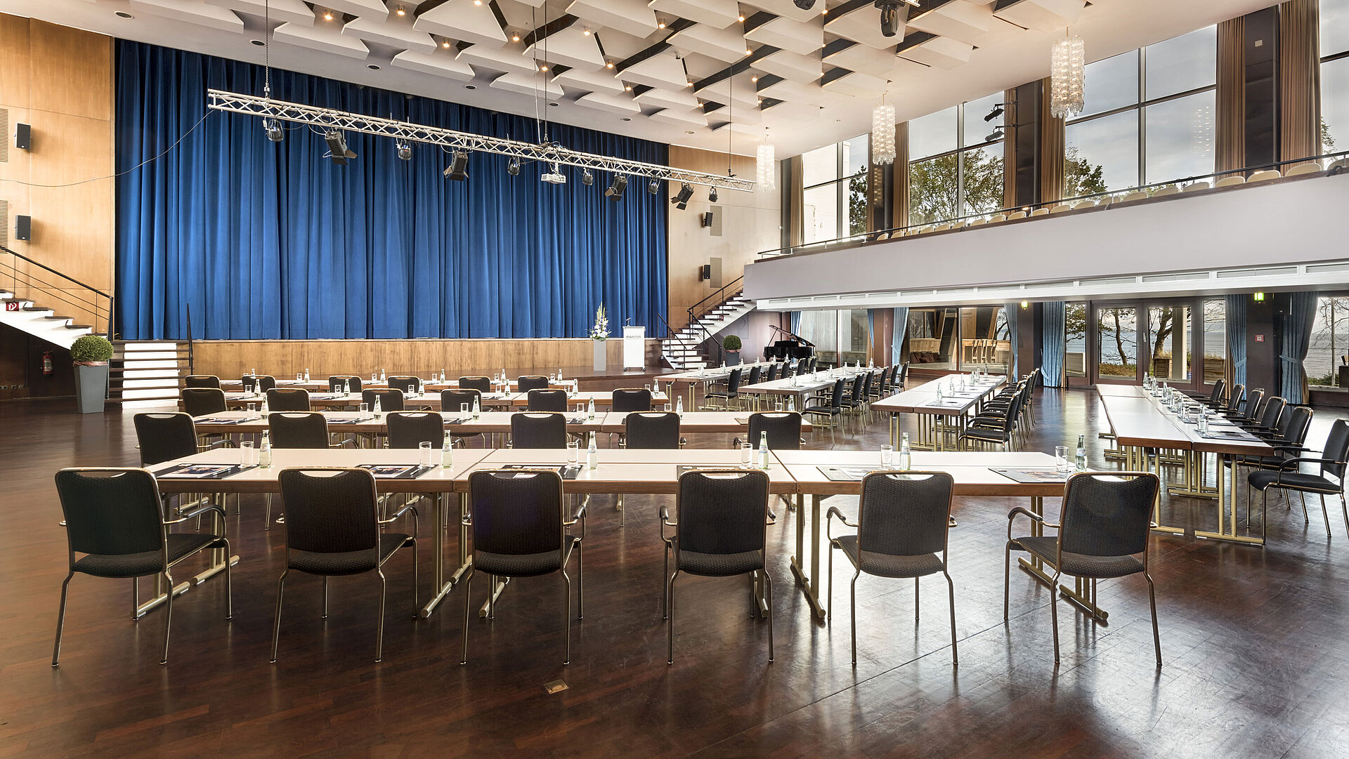 Gran sala «Maritim» en el Maritim Seehotel Timmendorfer Strand con escenario, cortinas azules y asientos para reuniones.