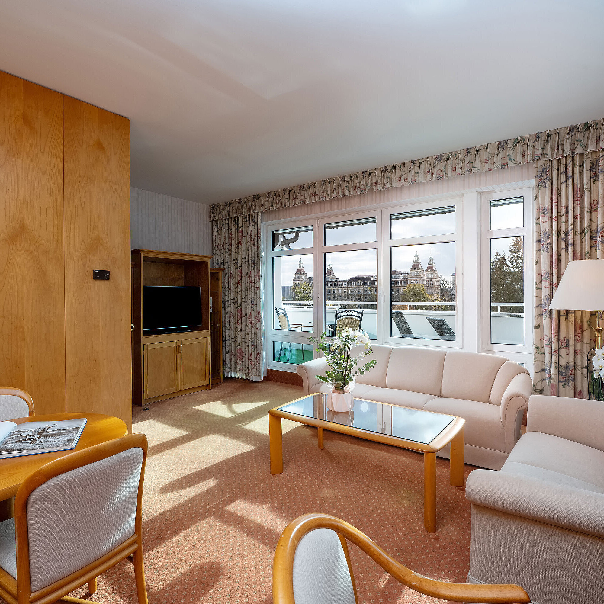 Junior Suite with bright living area, sofa, large window, dining space and classic interior at the Maritim Hotel.