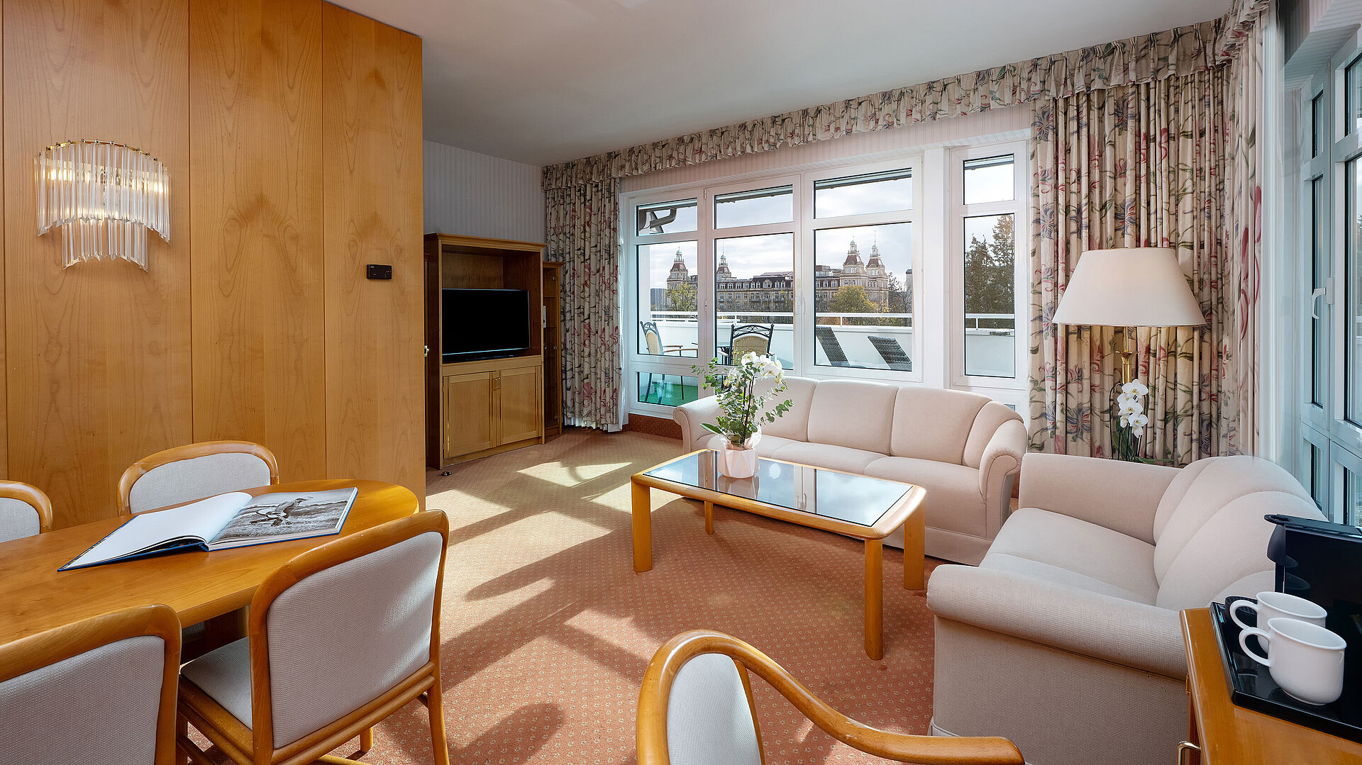 Suite Junior con sala de estar luminosa, sofá, gran ventana, zona de comedor y decoración clásica.