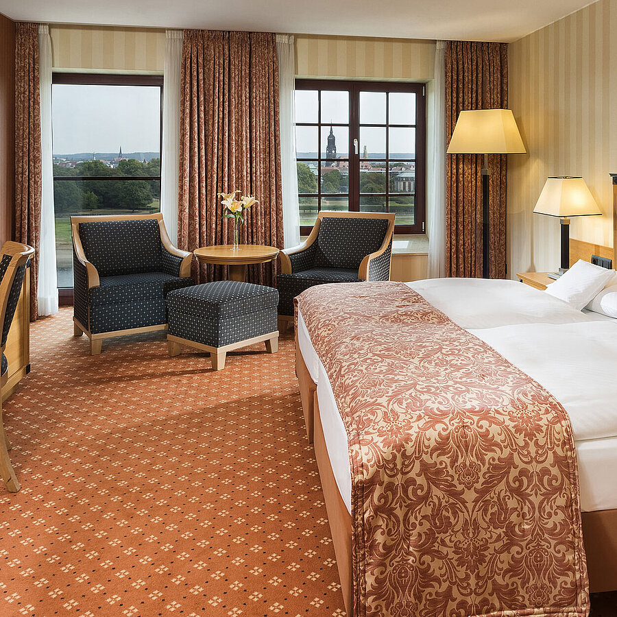 Chambre supérieure à l'hôtel Maritim de Dresde avec lit double élégant, bureau et coin salon avec vue sur la ville.