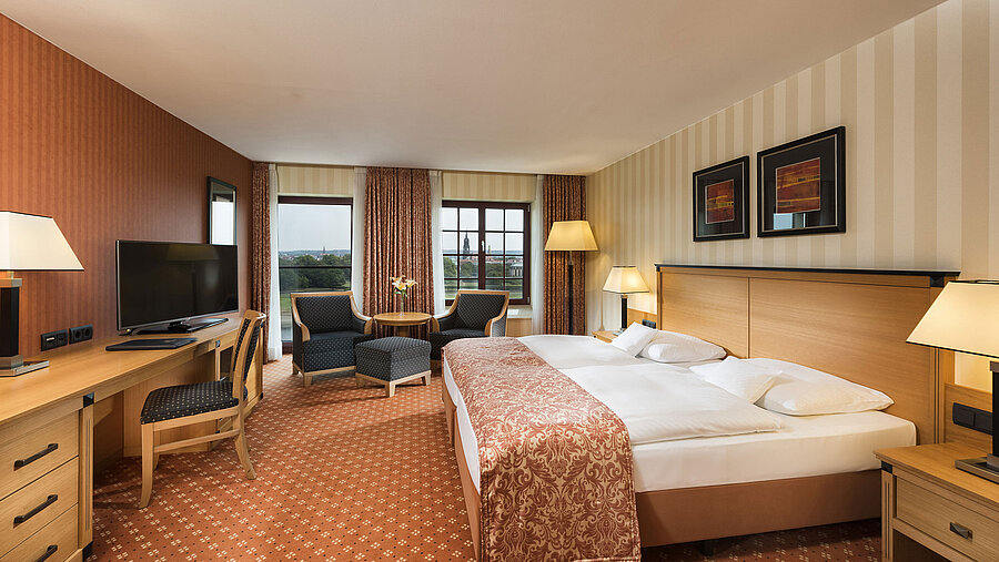Chambre supérieure à l'hôtel Maritim de Dresde avec lit double élégant, bureau et coin salon avec vue sur la ville.