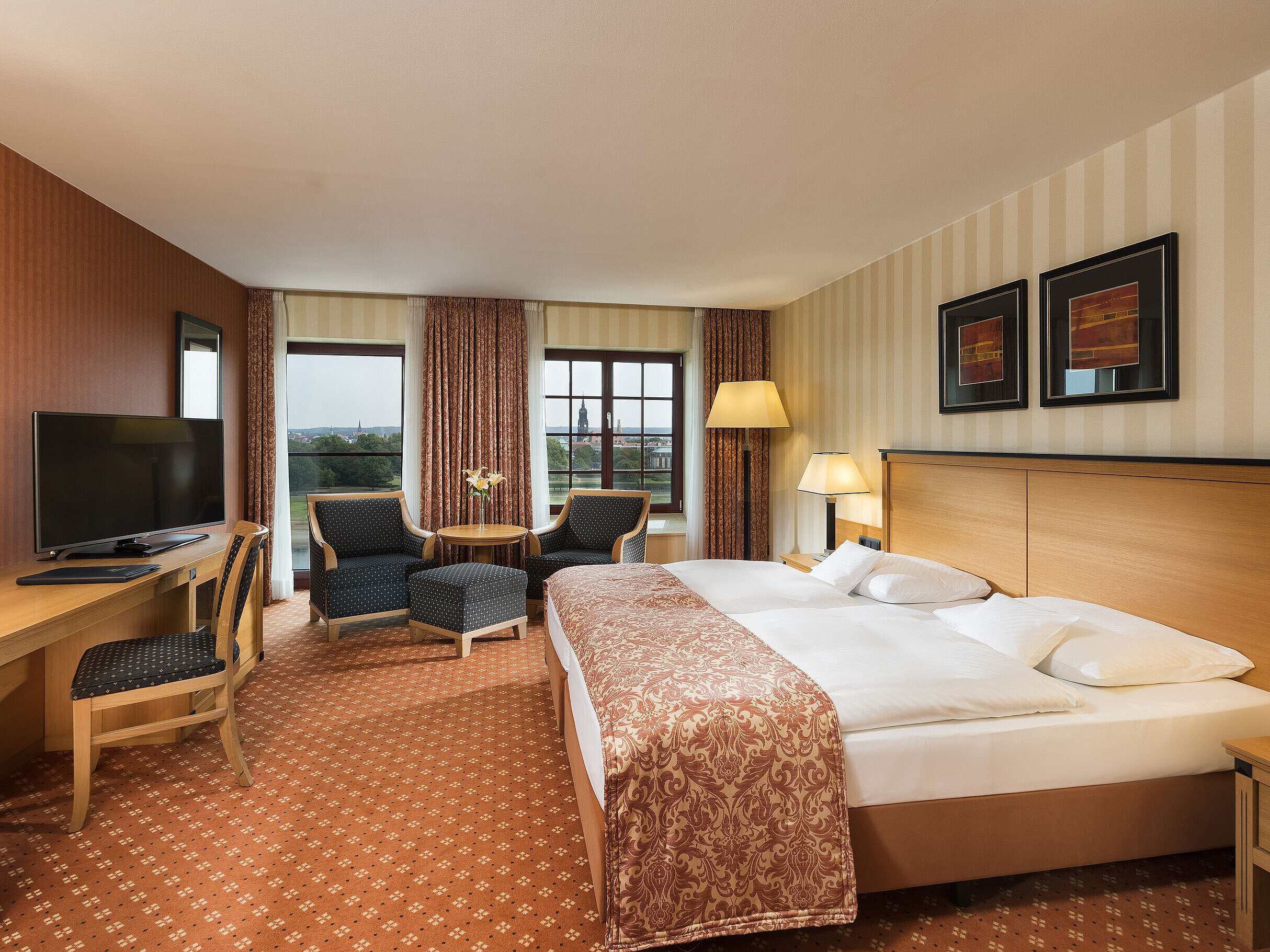 Chambre supérieure à l'hôtel Maritim de Dresde avec lit double élégant, bureau et coin salon avec vue sur la ville.