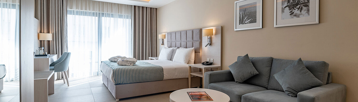 Suite Junior Spaziosa Junior Suite del Maritim Antonine Hotel & Spa Malta con zona giorno e notte combinata, divano e comodo letto matrimoniale.