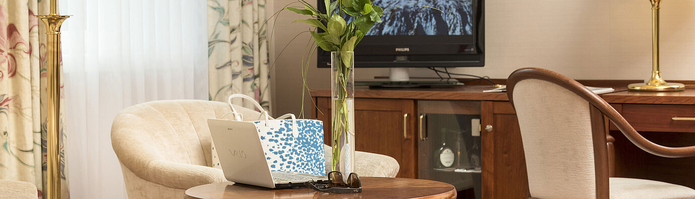 Coin salon avec roses, ordinateur portable et TV dans une chambre du Maritim Hotel Bad Wildungen