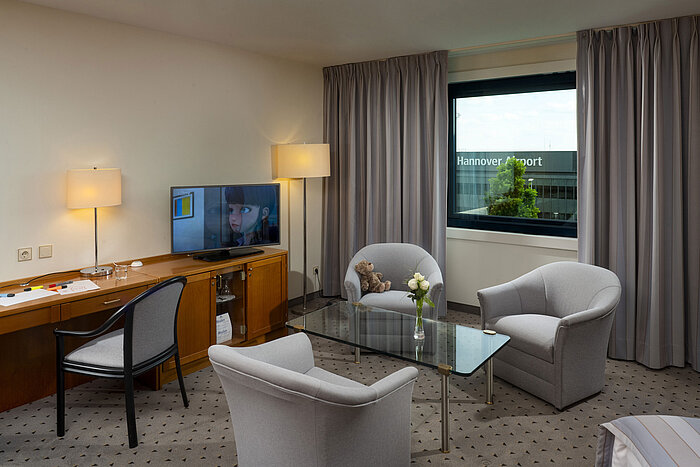 Habitación familiar cómoda con zona de estar, TV y vista al aeropuerto de Hannover en el Maritim Hotel Hannover.
