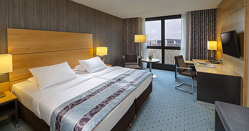 Comfort room at Maritim Hotel Düsseldorf with a large double bed, desk, armchair, and panoramic window.