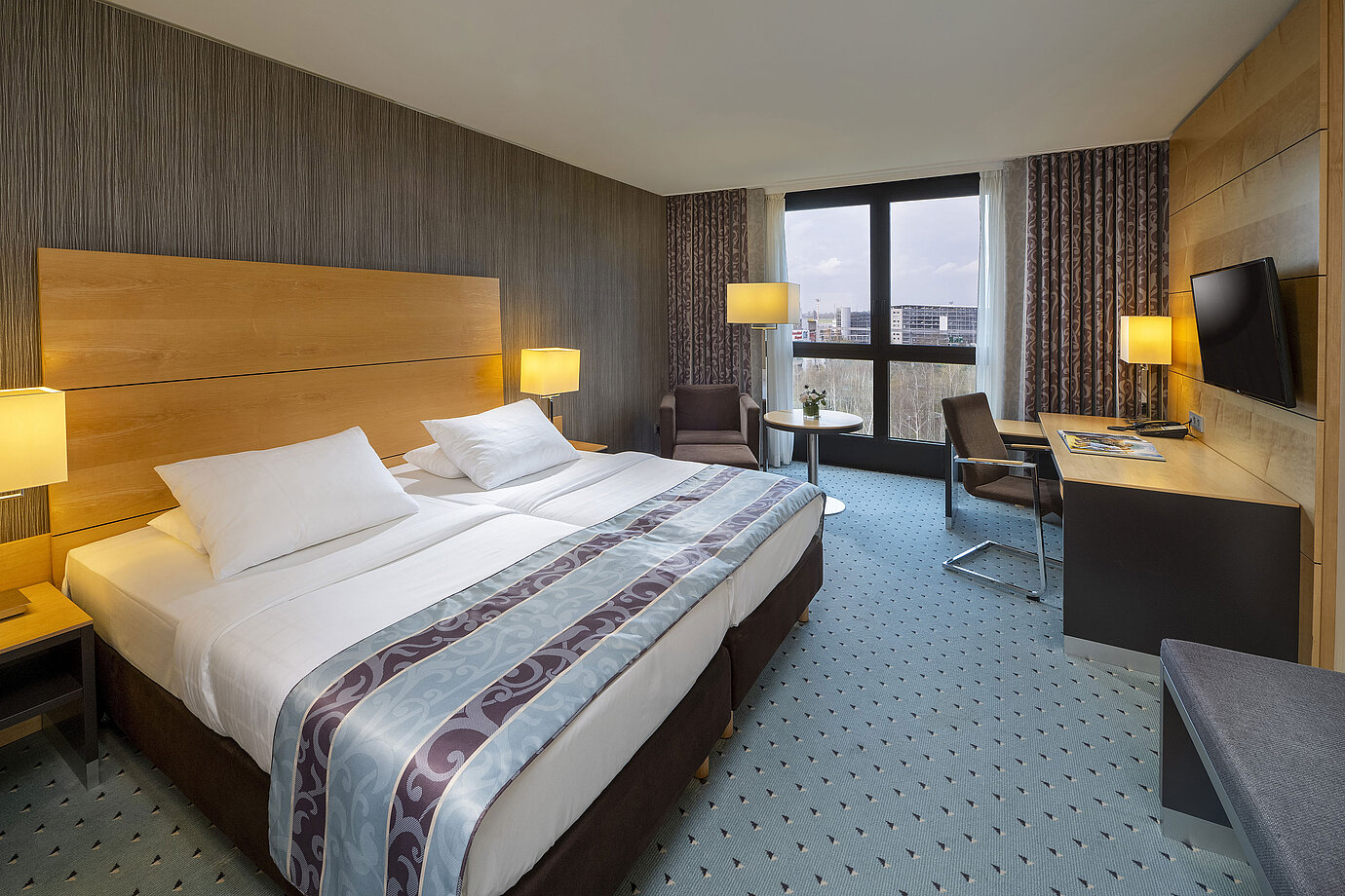 Habitación comfort en el Maritim Hotel Düsseldorf con cama doble grande, escritorio, sillón y ventana panorámica.
