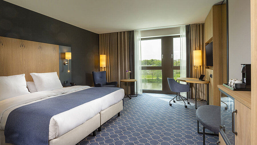 Spacious double room at Maritim Hotel Ingolstadt with large bed, desk, and a view of the river.