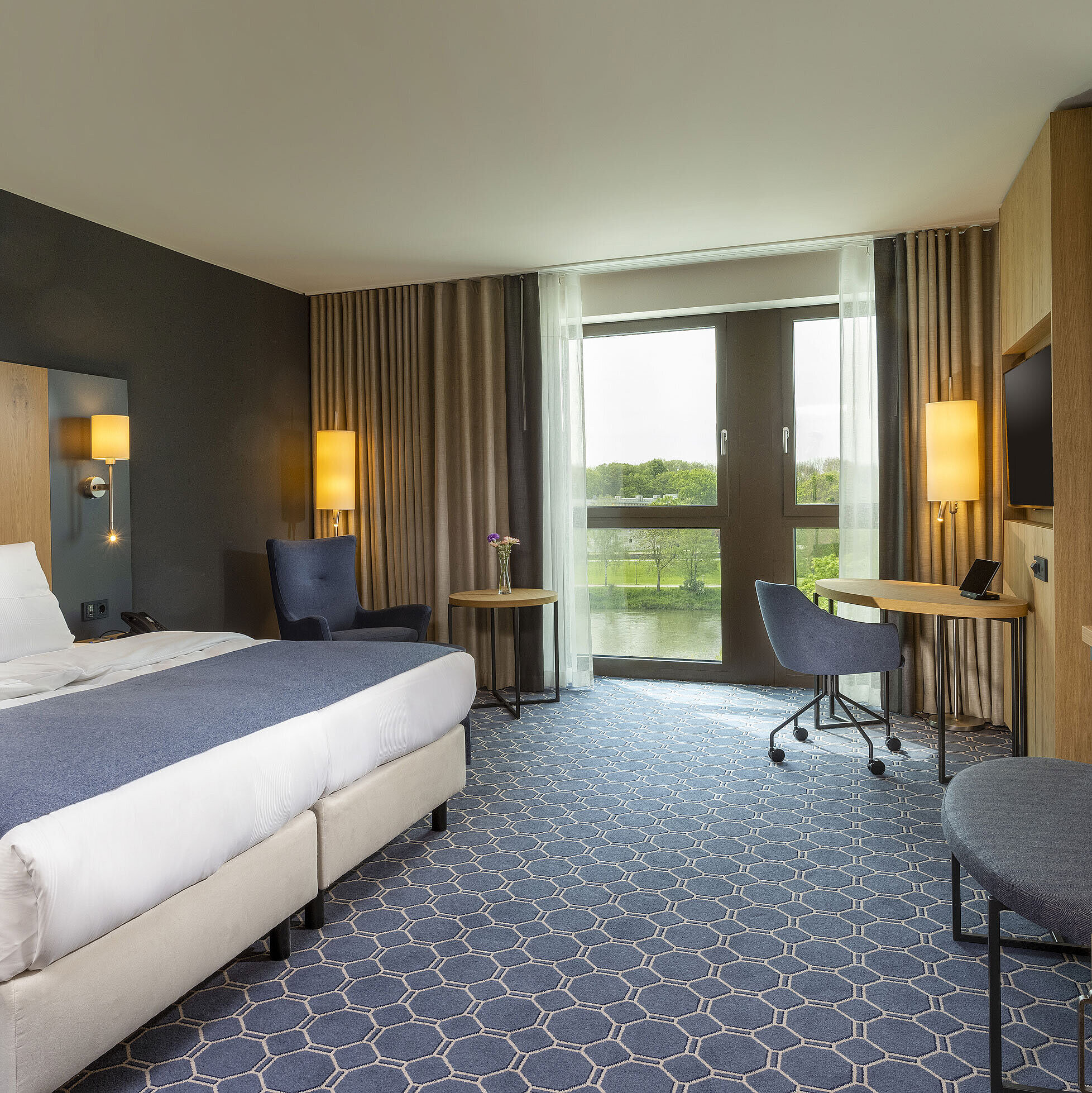 Spacious double room at Maritim Hotel Ingolstadt with large bed, desk, and a view of the river.