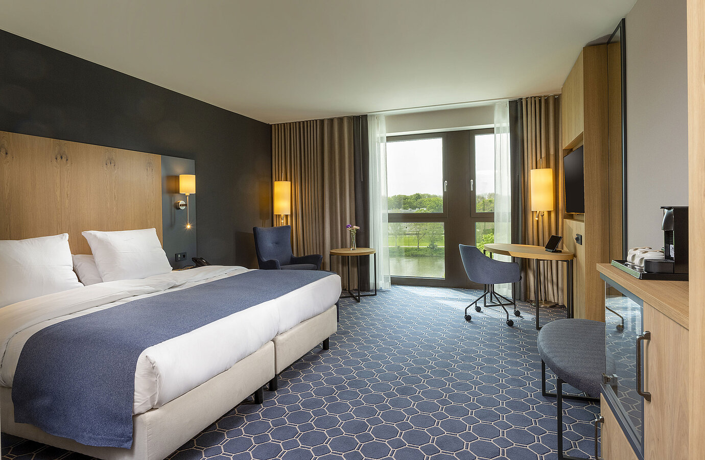 Spacious double room at Maritim Hotel Ingolstadt with large bed, desk, and a view of the river.