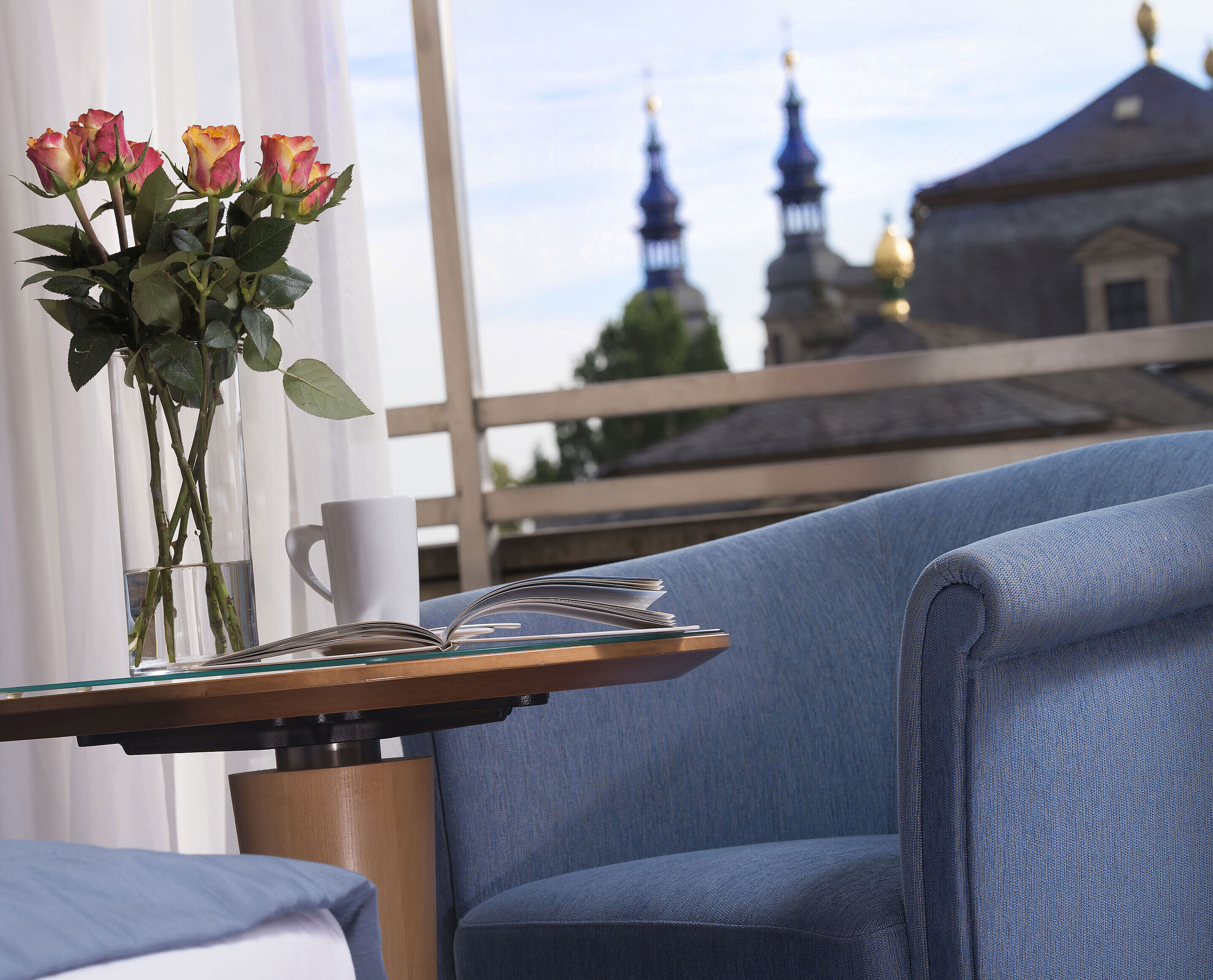 Elegante dettaglio di camera al Maritim Hotel Fulda con seduta blu, rose e vista sulle torri barocche di Fulda.