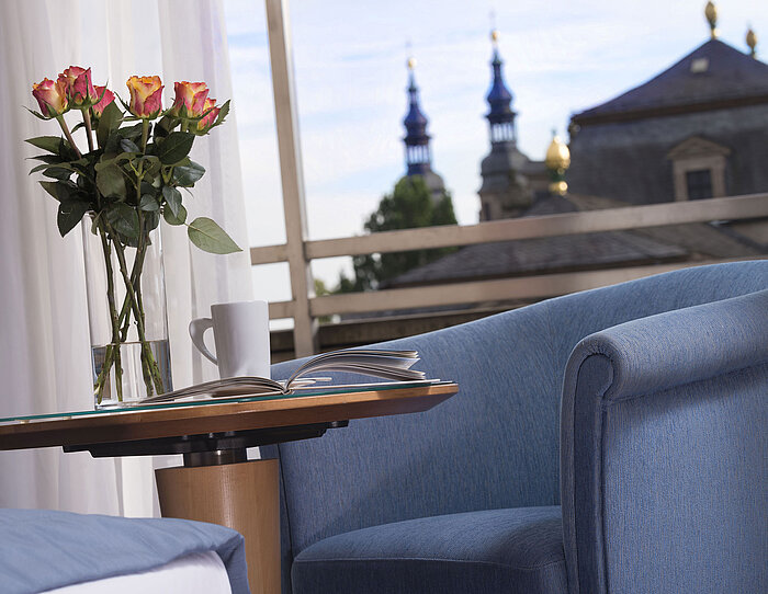 Elegante dettaglio di camera al Maritim Hotel Fulda con seduta blu, rose e vista sulle torri barocche di Fulda.