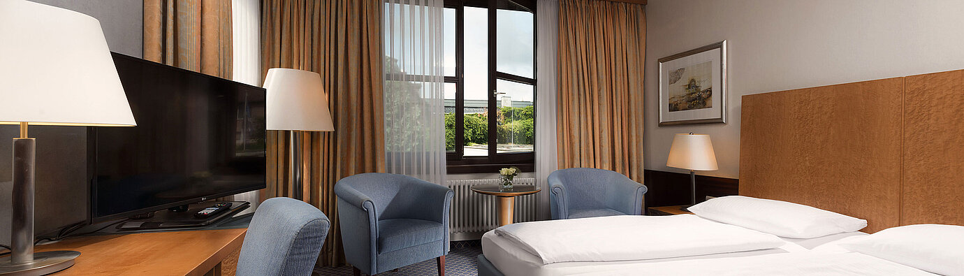 Classic room at Maritim Hotel Fulda with a cozy double bed, desk, seating area, and large window.