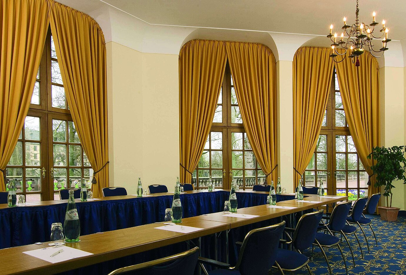 Salle de réunion élégante avec grandes fenêtres, rideaux dorés et lustre à l'hôtel Maritim Fulda.