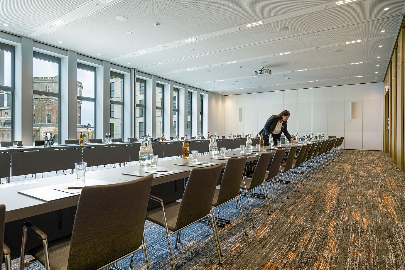 Employée préparant une salle de réunion moderne à l'hôtel Maritim Ingolstadt. Grandes fenêtres avec vue sur la ville.