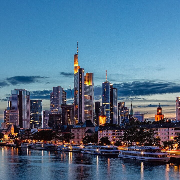 View across the River Main towards the illuminated Frankfurt skyline at dusk.