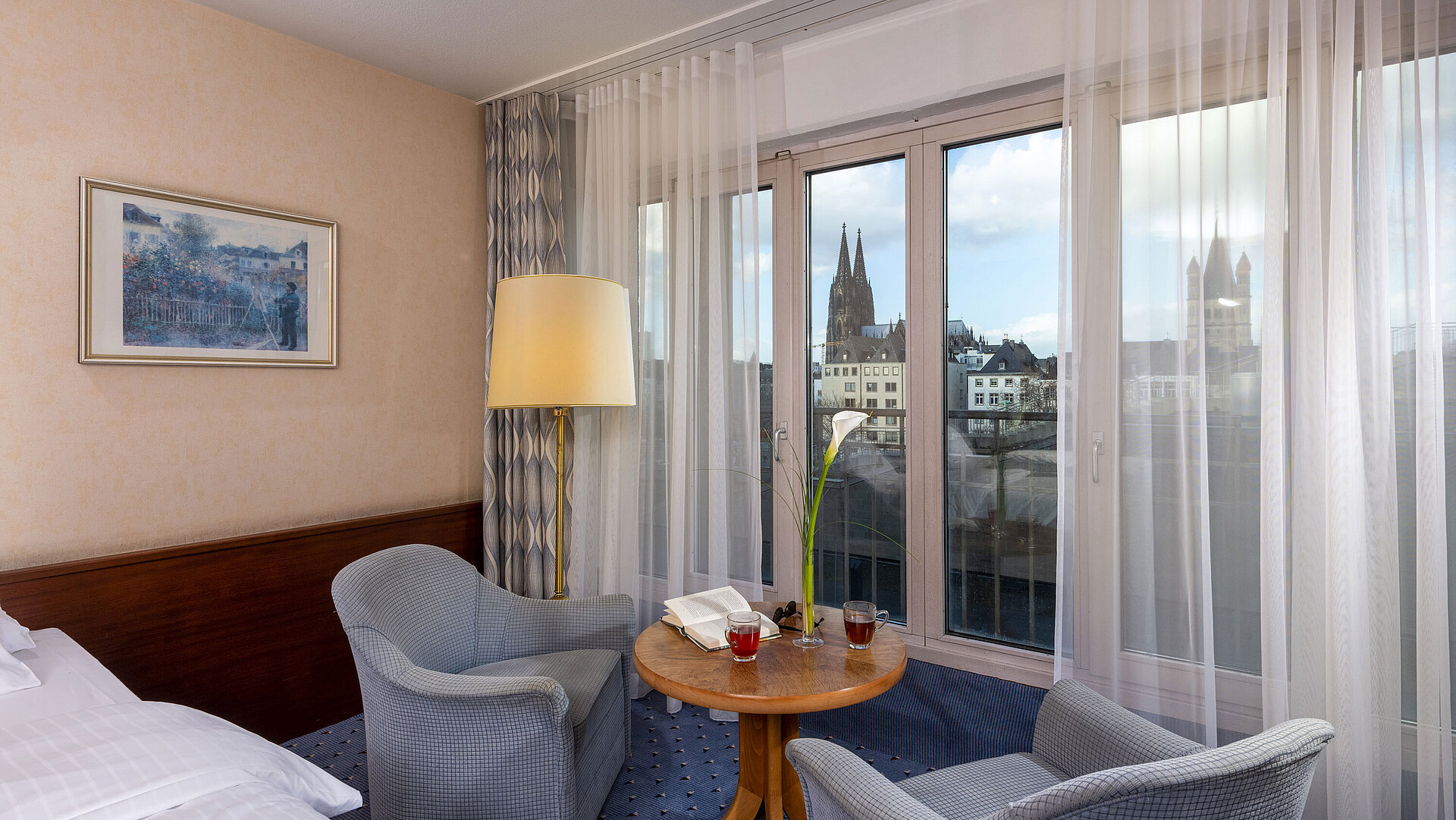 Standard Twin room at Maritim Hotel Cologne with two chairs, a table, large window, and view of Cologne Cathedral.