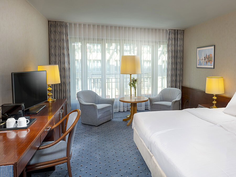 Classic room at the Maritim Hotel Cologne with a double bed, cozy seating area, desk, and TV.