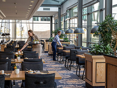 Intérieur lumineux du restaurant Wintergarten au Maritim Hotel Dresden avec grandes baies vitrées et tables dressées.