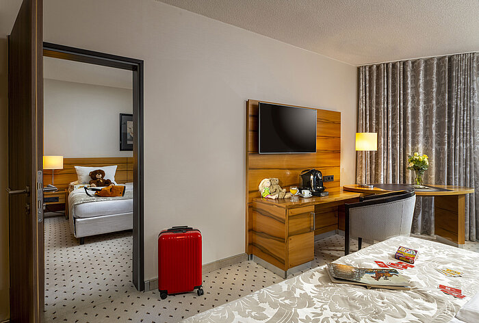 Chambre familiale à l'hôtel Maritim Bad Homburg avec chambre séparée pour enfants, peluches et valise rouge.