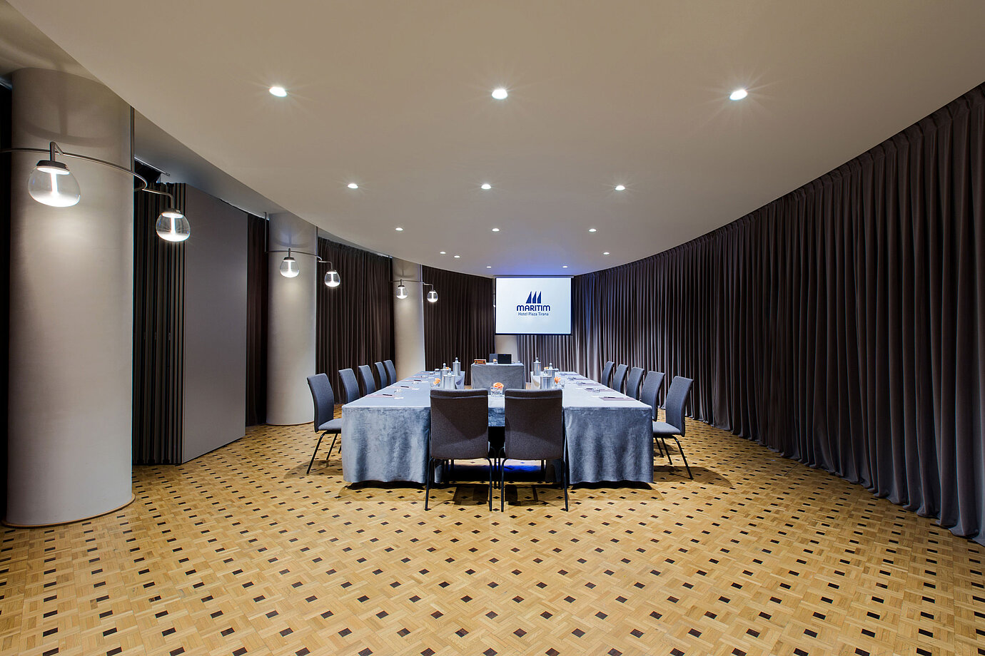 Sala de reuniones moderna en Maritim Hotel Plaza Tirana con disposición en U, pantalla y cortinas elegantes